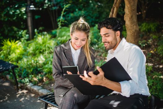 Two business professionals discussing documents outdoors in a park setting.