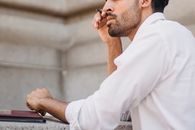 一名身穿白衬衫的男子若有所思地拿着笔，侧影映在外面