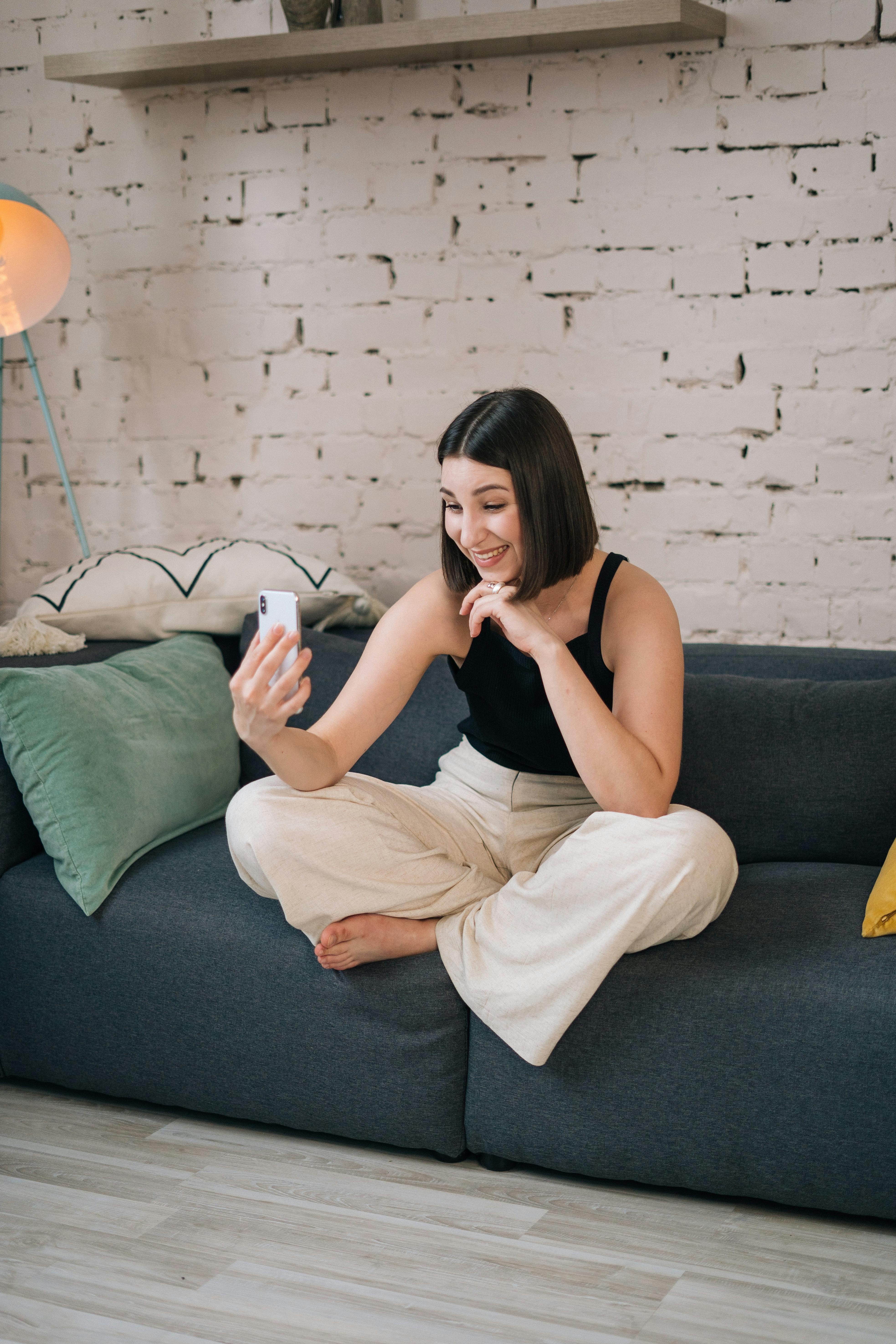 girl in black tank top and white pants sitting on gray couch