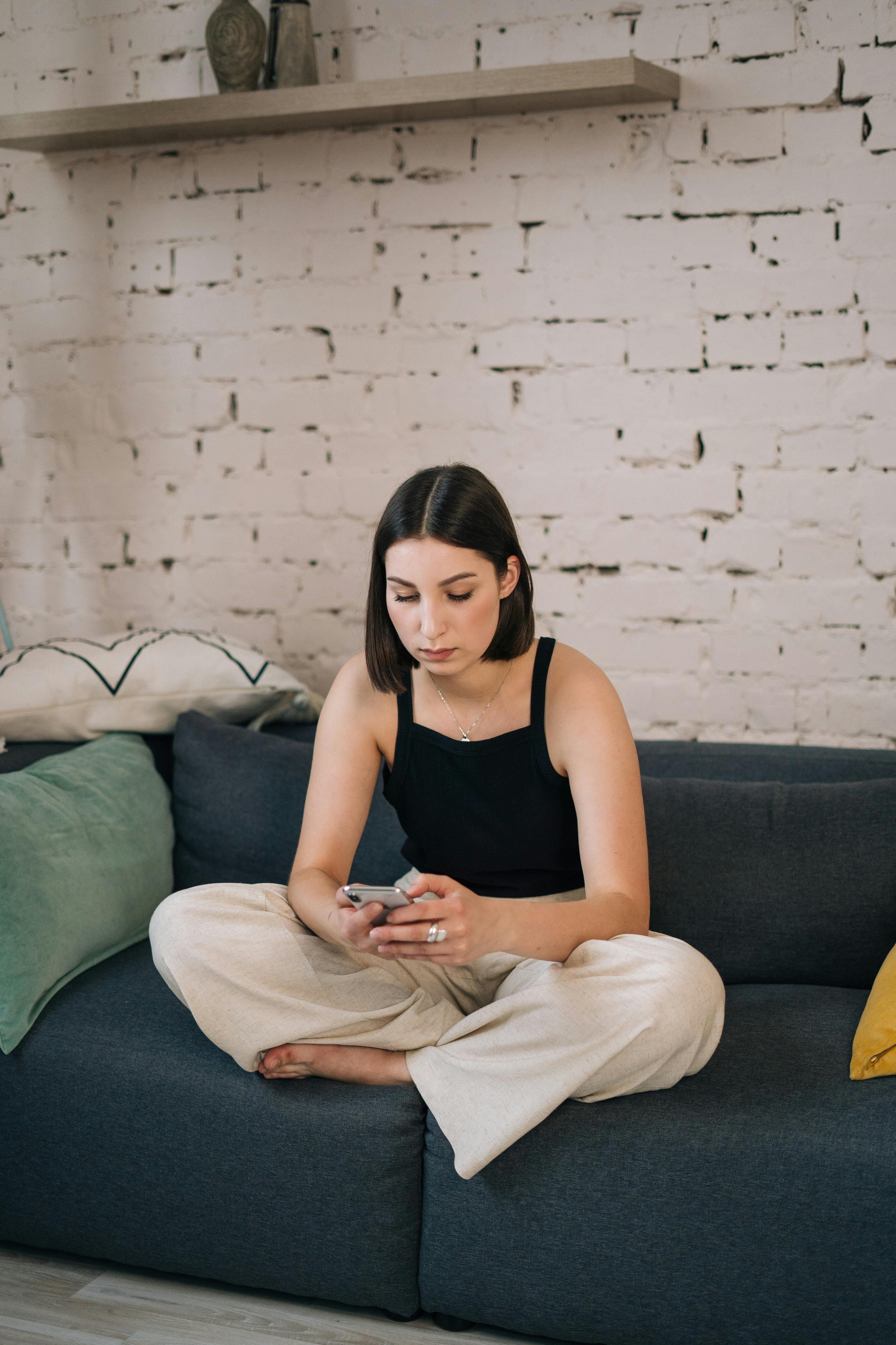 woman sitting on the sofa while using her smartphone