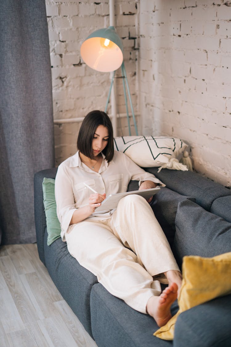 Woman In White Long Sleeves Sitting On The Gray Couch