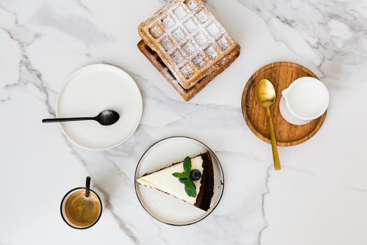 Top view of waffles and cheesecake with coffee on a marble table. Perfect for gourmet dining visuals.