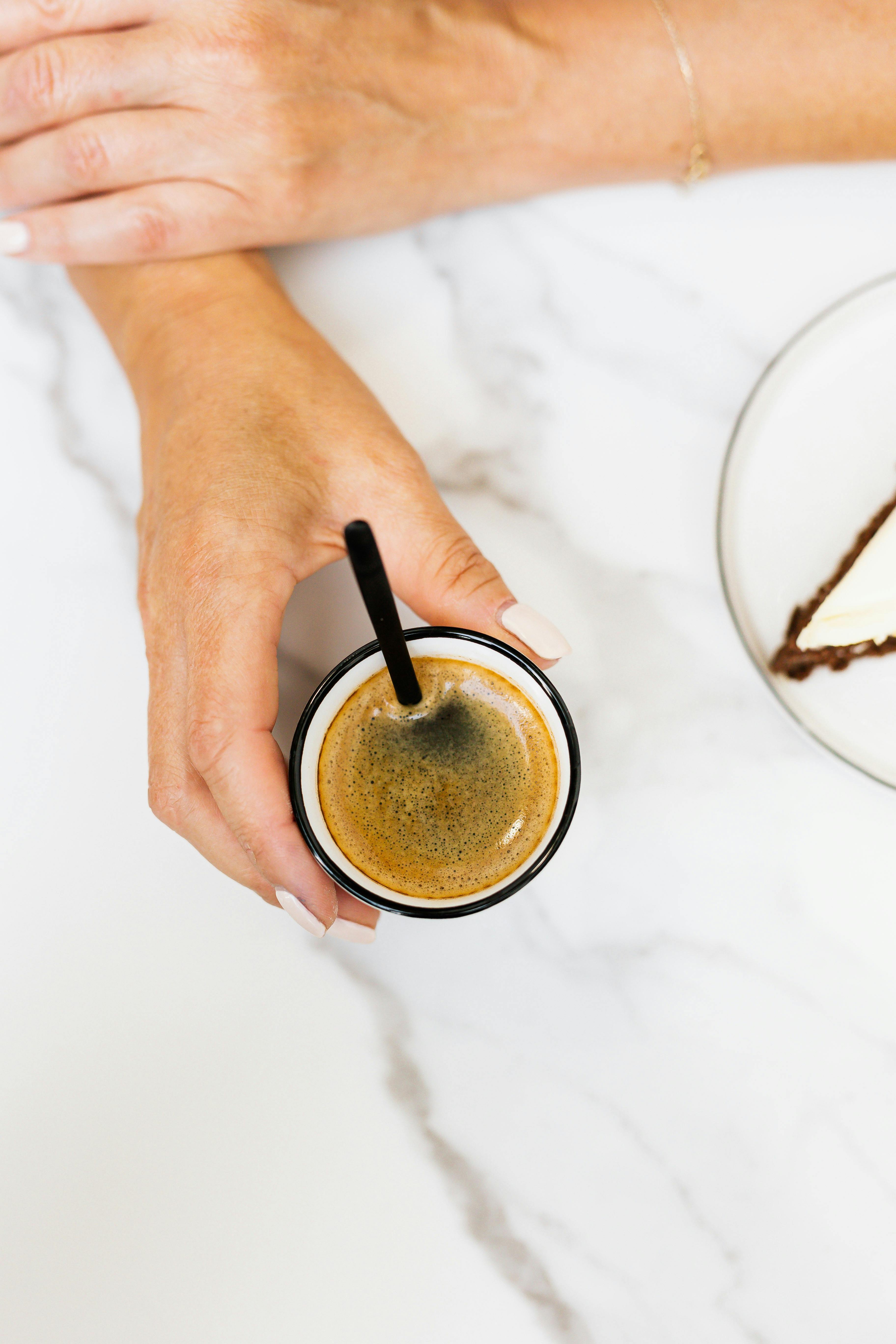 一只手持着浓缩咖啡杯，优雅地置于一张摆有甜点盘的大理石桌上