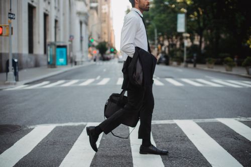 Free A businessman crosses a city street with jacket in hand, portraying urban elegance. Stock Photo