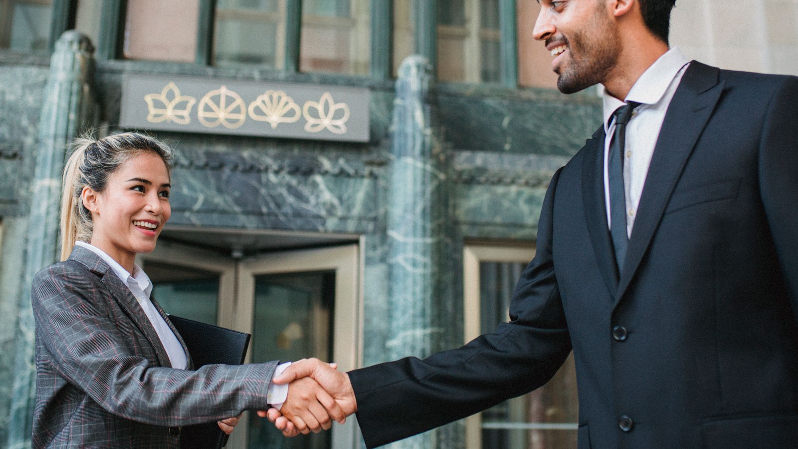 Two business professionals shaking hands confidently outside a modern building.