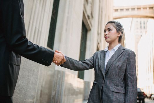 Two business professionals shaking hands outdoors in urban setting, symbolizing partnership.