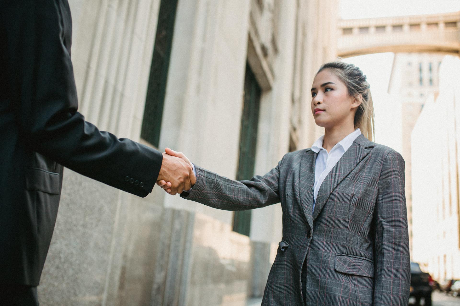 Two business professionals shaking hands outdoors in urban setting, symbolizing partnership.