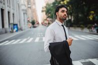 晴朗的日子里，一位自信的商人拿着西装外套，穿过城市街道