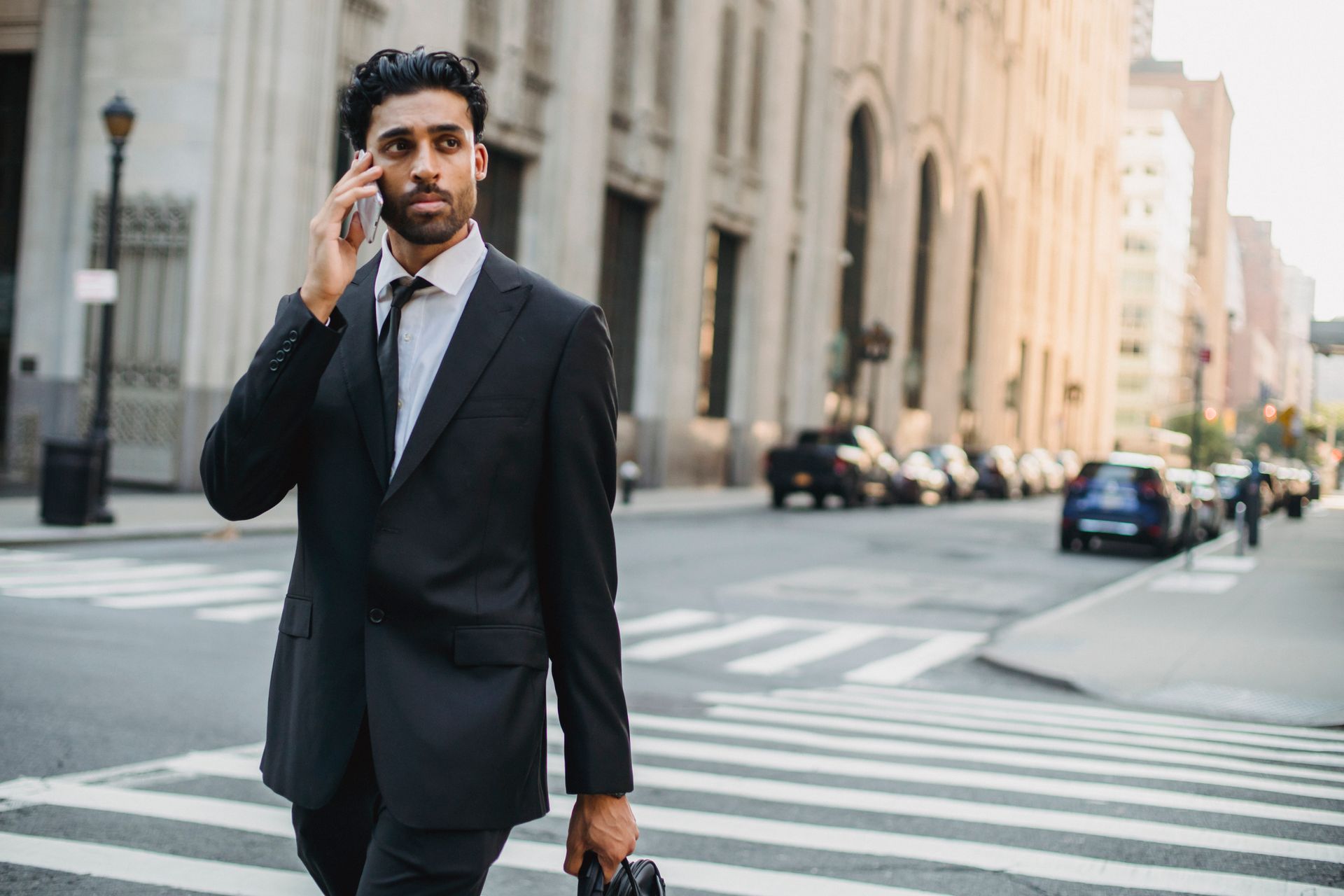 A professional man in a suit walking and talking on the phone in an urban street setting.