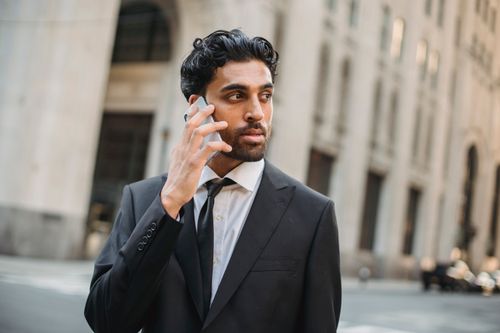 Free Stylish businessman in black suit talking on smartphone outdoors in urban setting, exuding confidence. Stock Photo