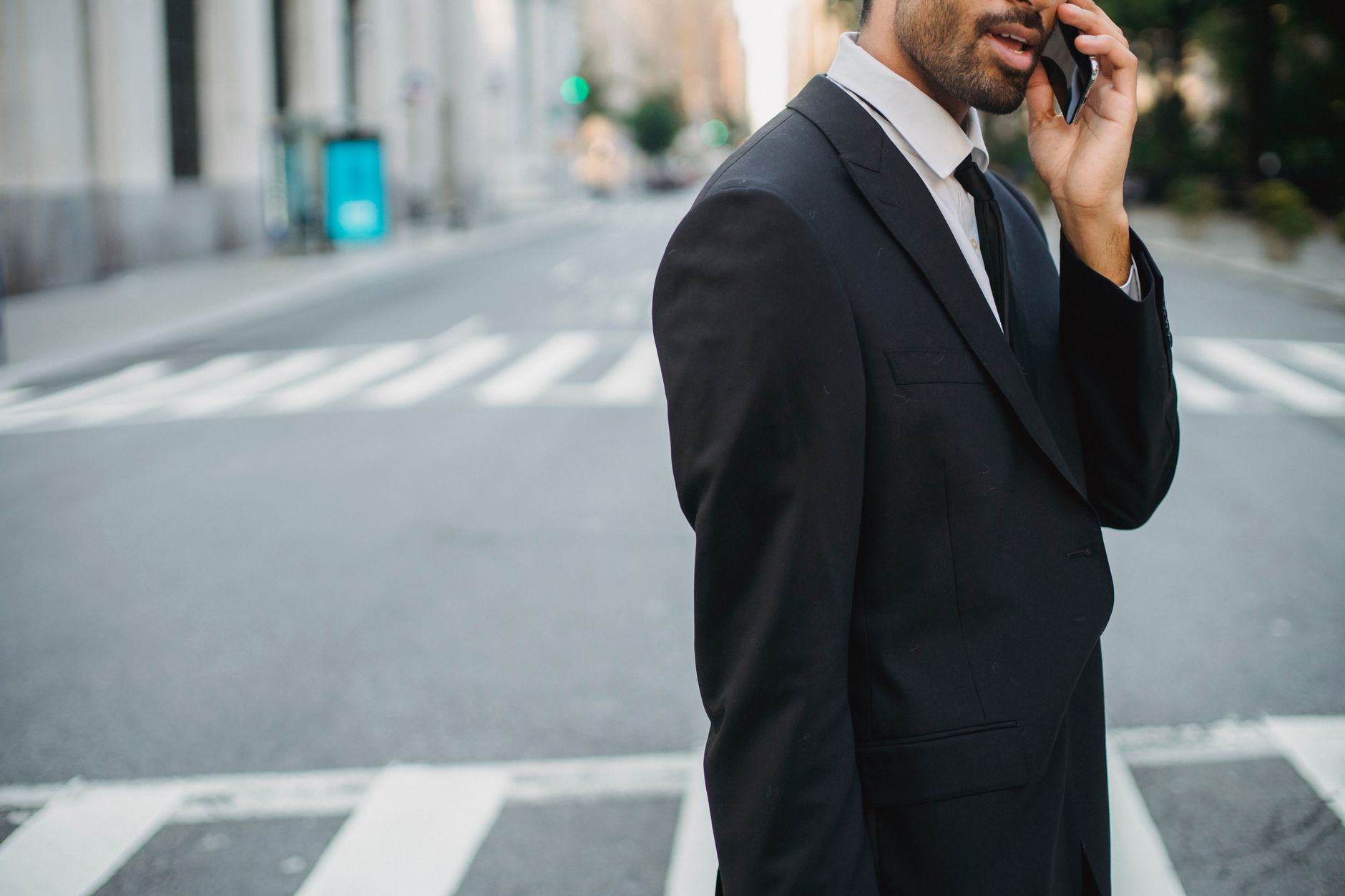 Young businessman talking on mobile phone in a city street wearing a black suit.
