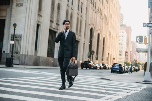 一位穿着西装的自信商人正一边穿过城市街道一边打电话