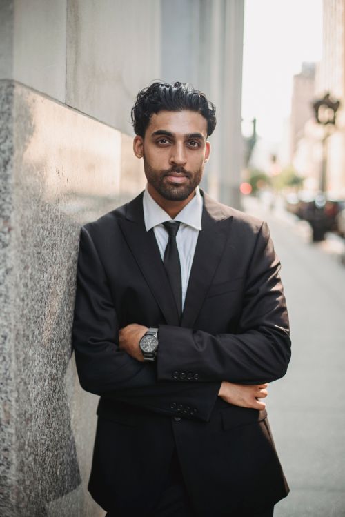 Free Stylish young man in a suit leans against a wall on a city street, exuding confidence. Stock Photo