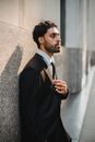 一名穿着正式西装的成年男子自信地靠在户外墙边摆姿势