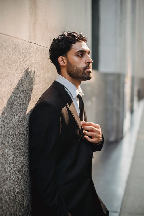 Free An adult man in a formal suit poses confidently against a wall outdoors. Stock Photo
