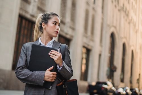 Free A professional woman in a suit holds a folder on a city street, exuding confidence. Stock Photo