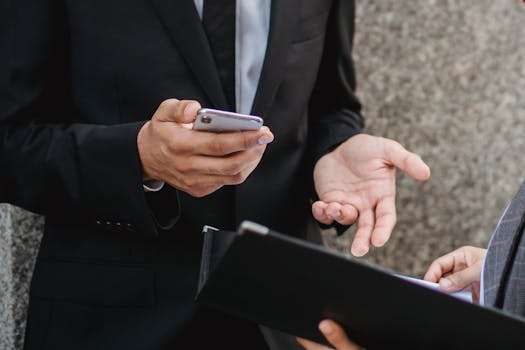 Close-up of business professionals discussing deals with a smartphone and documents, emphasizing communication and collaboration.