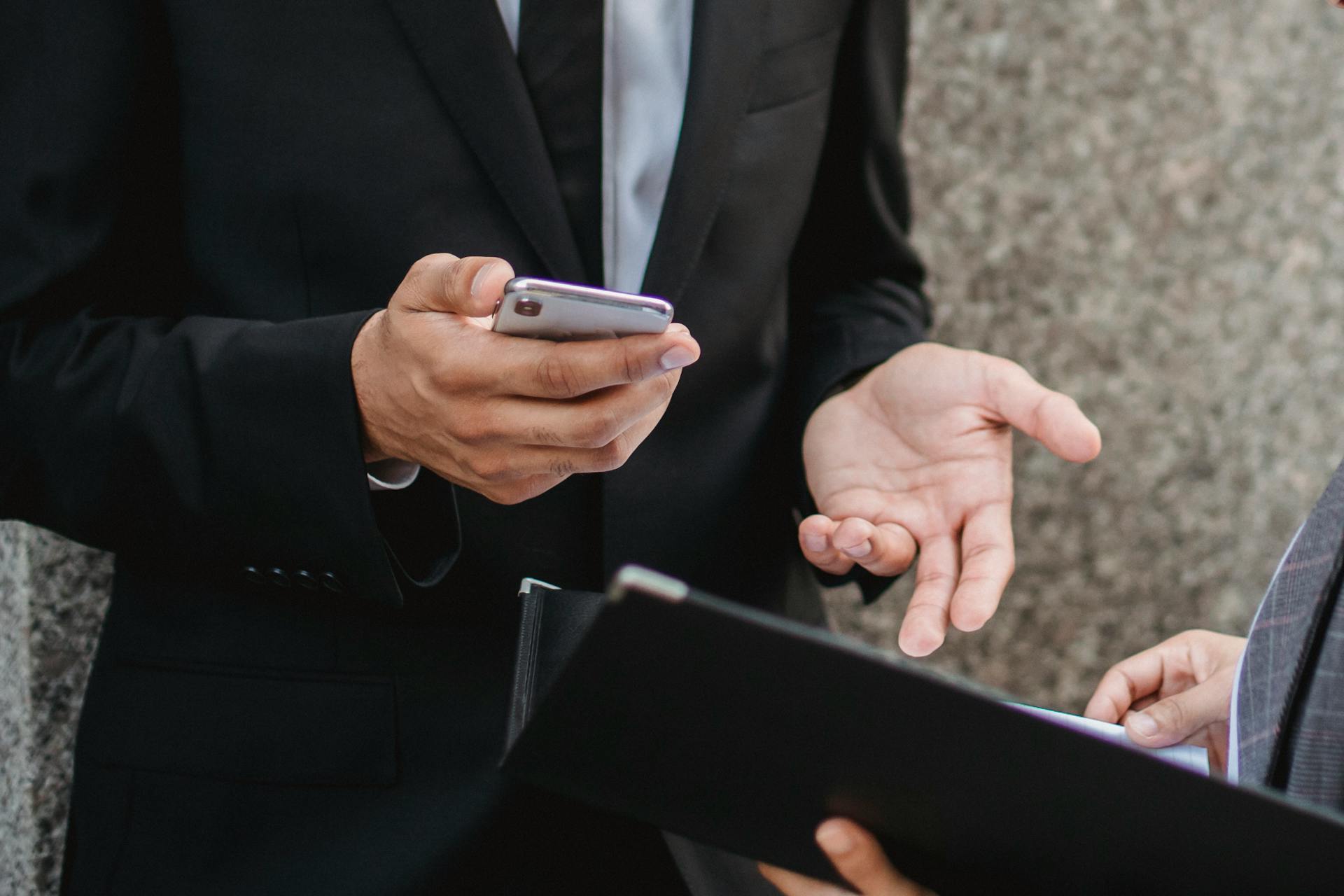 Close-up of business professionals discussing deals with a smartphone and documents, emphasizing communication and collaboration.