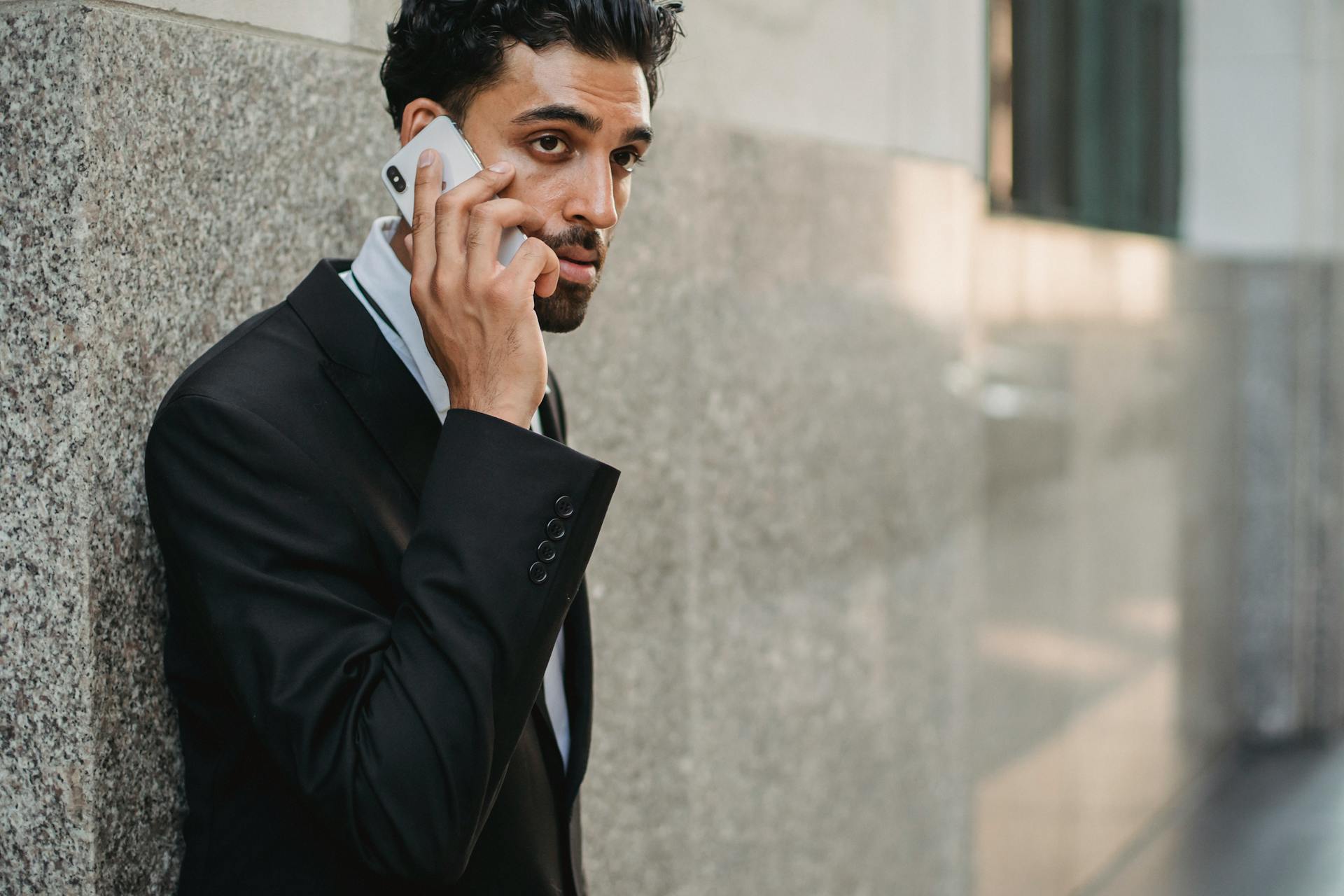 Professional businessman in a suit having a phone conversation outside office building.