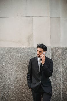 Confident businessman in a black suit making a call against a stone wall.