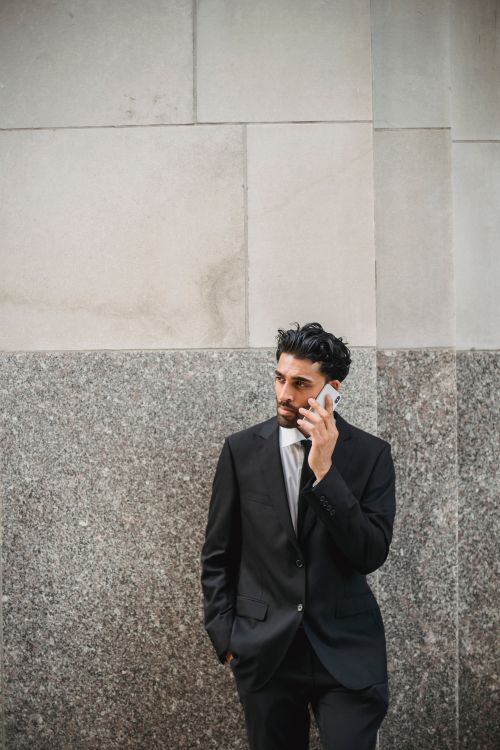 Free Confident businessman in a black suit making a call against a stone wall. Stock Photo