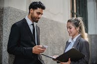 两名商务人士手持智能手机和文件，在建筑物外进行对话