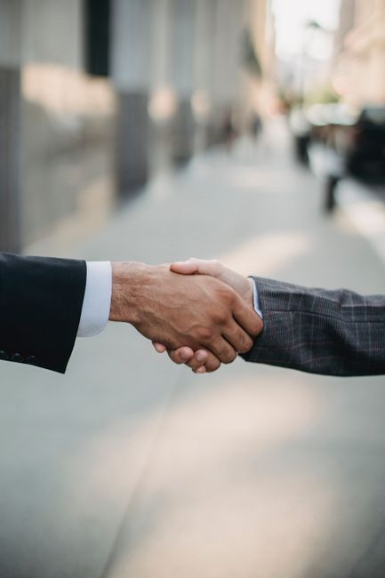 Two businessmen shaking hands outside, symbolizing cooperation and agreement in a city setting. Two businessmen shaking hands outside, symbolizing cooperation and agreement in a city setting.