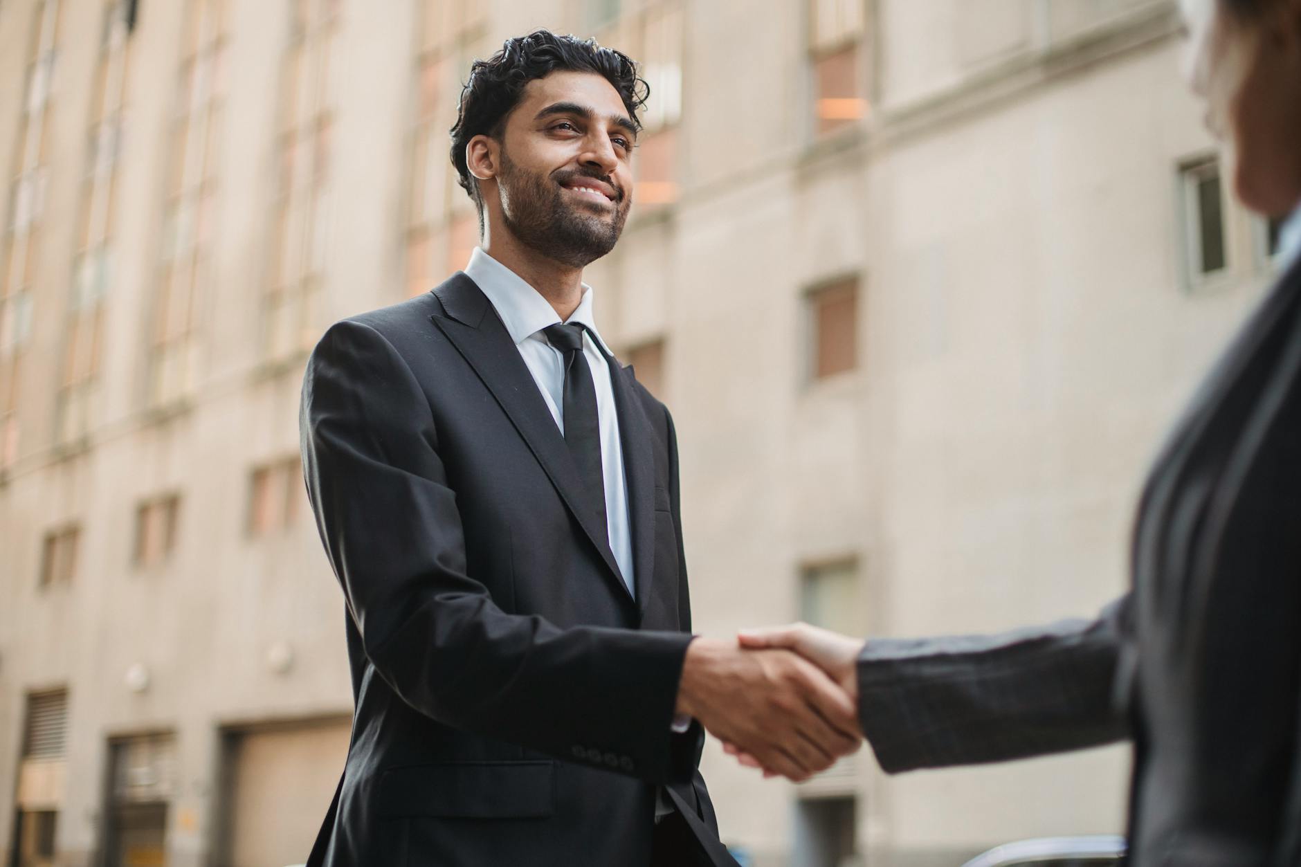 Business professionals in suits shaking hands outdoors, symbolizing agreement and partnership.