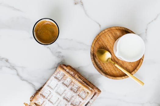 Aesthetic breakfast flat lay featuring a coffee cup, milk jug, and freshly baked waffle on marble.