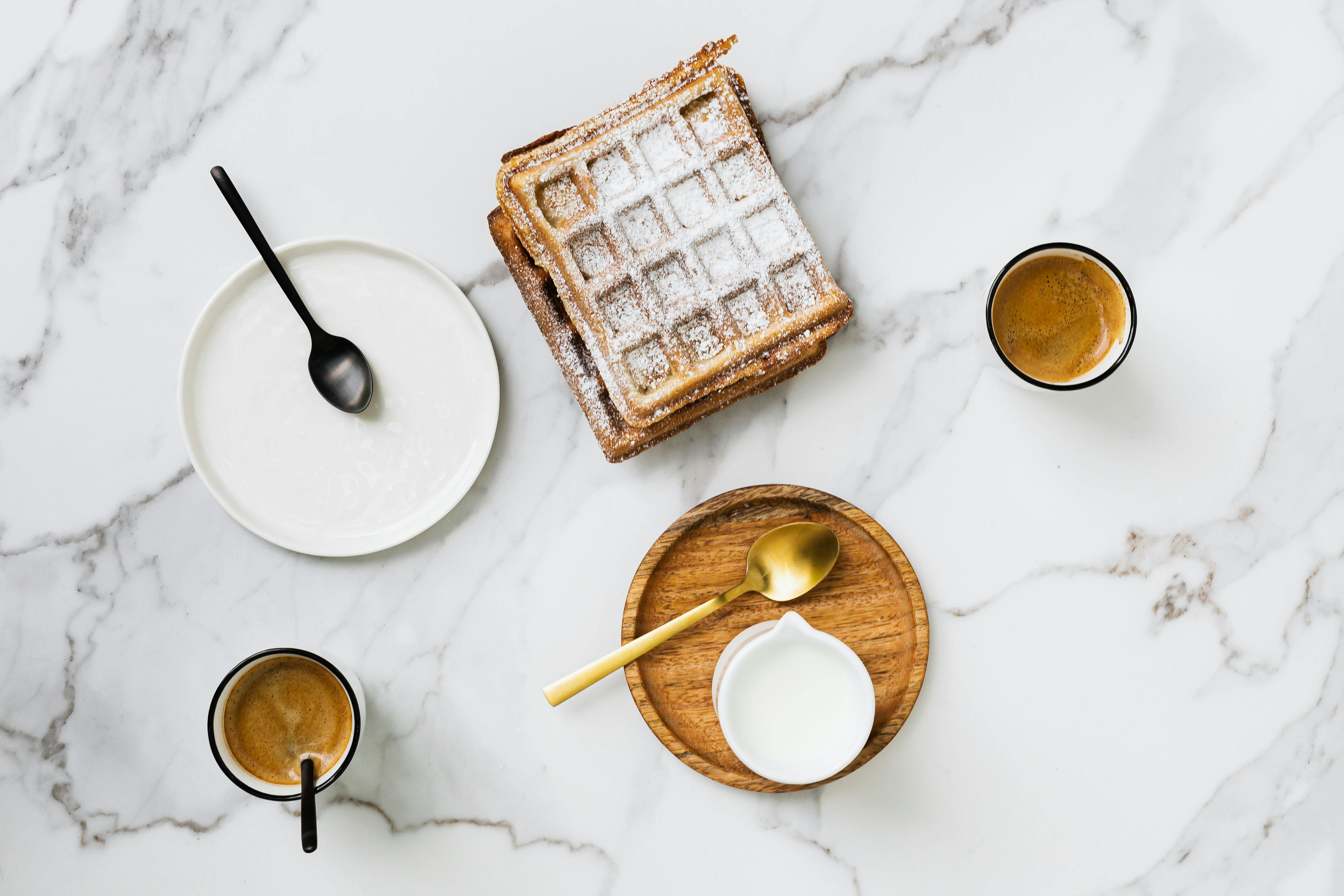 大理石表面的顶视图上，摆放着美味的华夫饼早餐、咖啡杯和牛奶