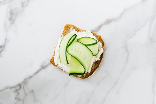 Free Top view of a bread slice with cream cheese and cucumber on a marble surface. Stock Photo