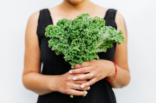 Free Close-up of a woman holding fresh kale, representing healthy living and nutrition. Stock Photo