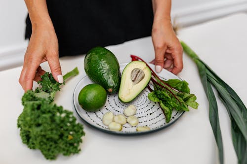 Person Holding White and Black Plate with Sliced Avocado and Green Vegetable