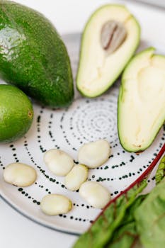 High-angle view of fresh avocado halves with broad beans and greens on a plate.