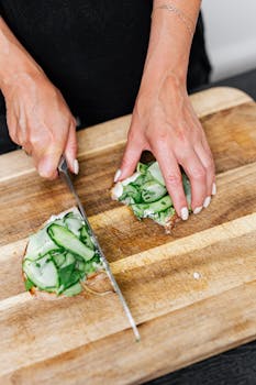 Hands slicing cucumber sandwich on wooden board, showcasing detailed food preparation.
