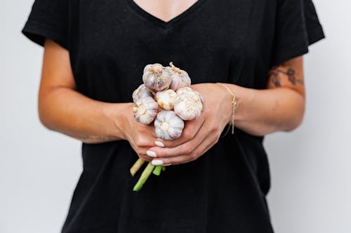 Photo of a Person in a Black Shirt Holding a Bunch of Garlic