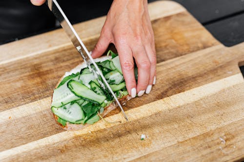 Free Close-up Photo of Person slicing Vegetable on a Wooden Chopping Board Stock Photo