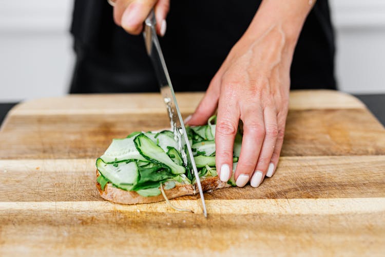 Photo Of A Person Slicing A Sandwich With Cucumber Slices