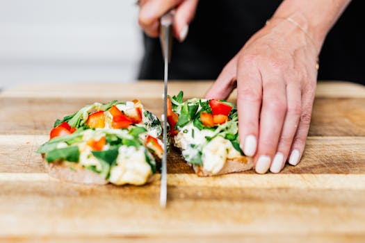 Close-up of hands slicing a fresh vegetable sandwich with various greens and red peppers.