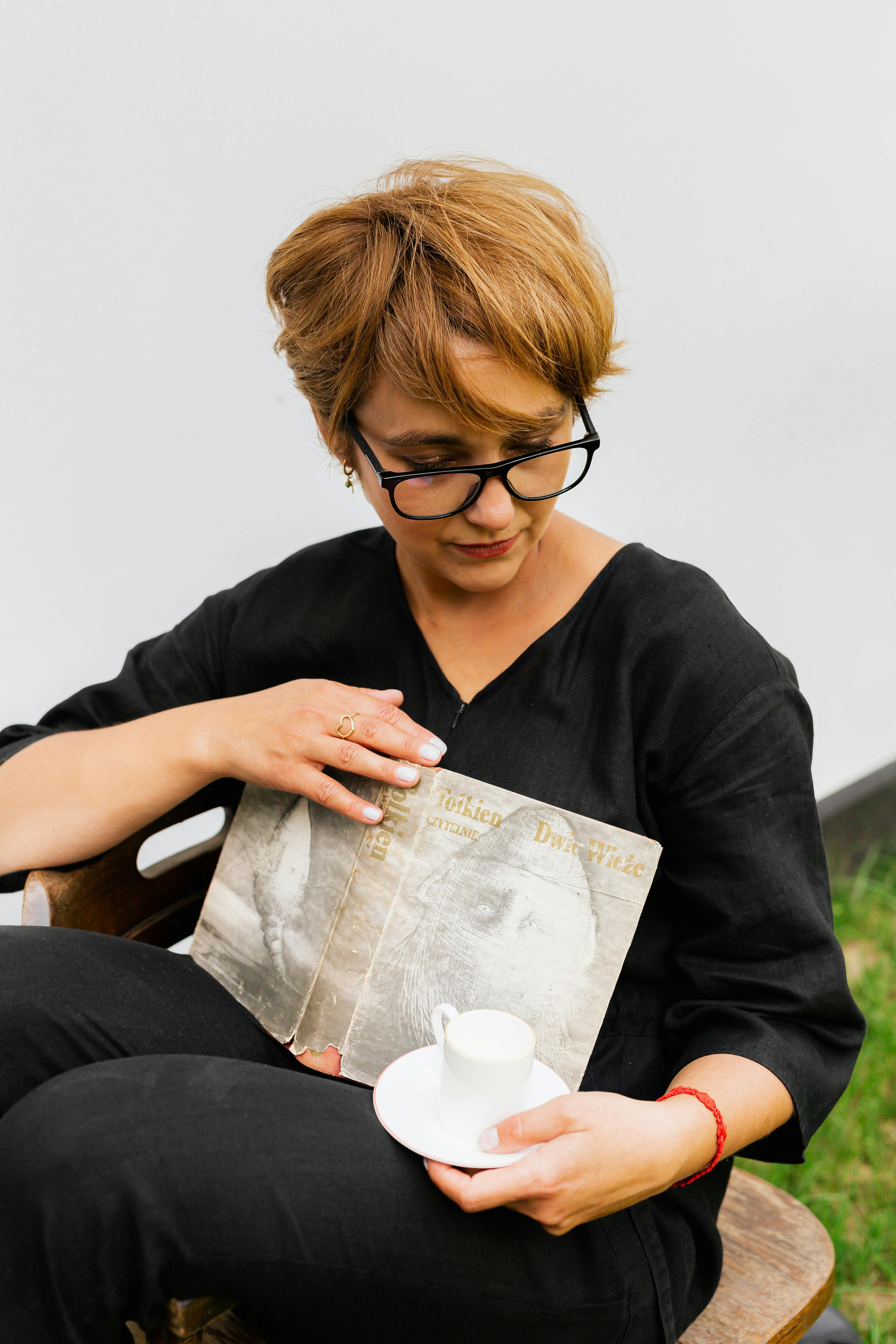 一位女士坐在户外，边喝咖啡边看书，享受着轻松休闲的时光