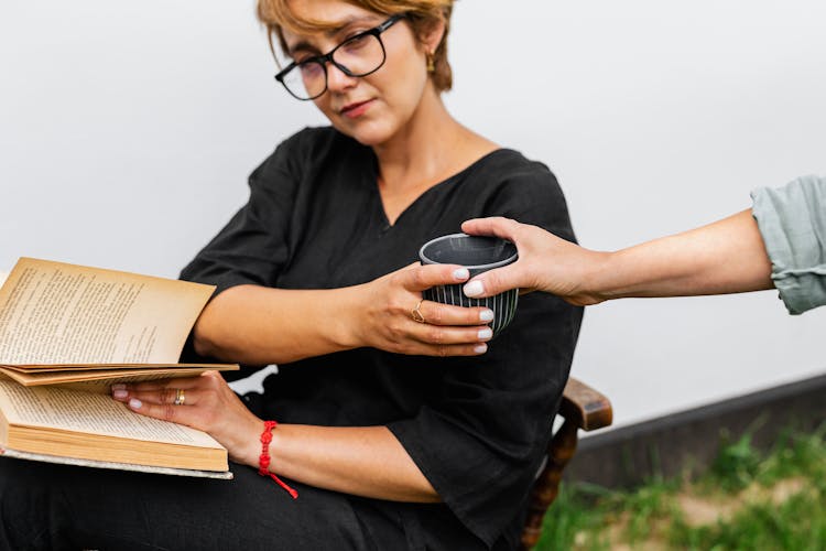 Hand Handing Cup To Woman Reading Book