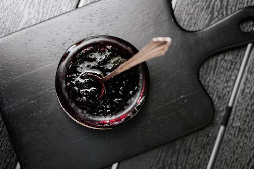Aerial shot of a jar of dark jam on a wooden board with a spoon
