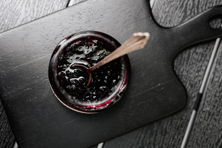 Aerial shot of a jar of dark jam on a wooden board with a spoon