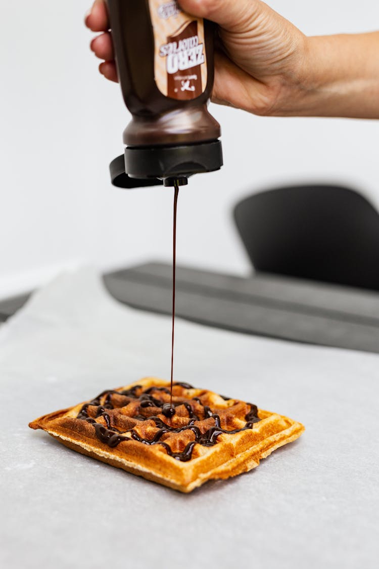 Person Pouring Chocolate Syrup On Brown Waffle