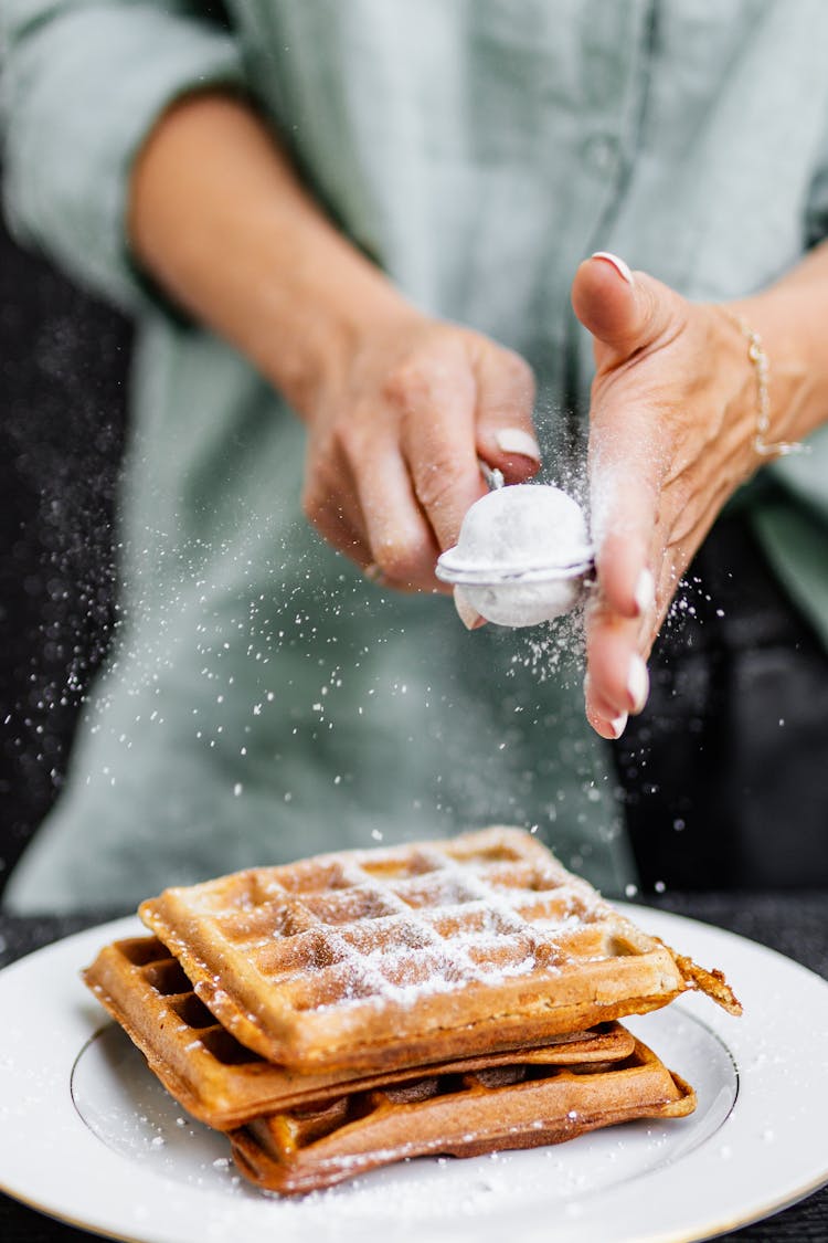 Person Sprinkling Powdered Sugar On Waffles