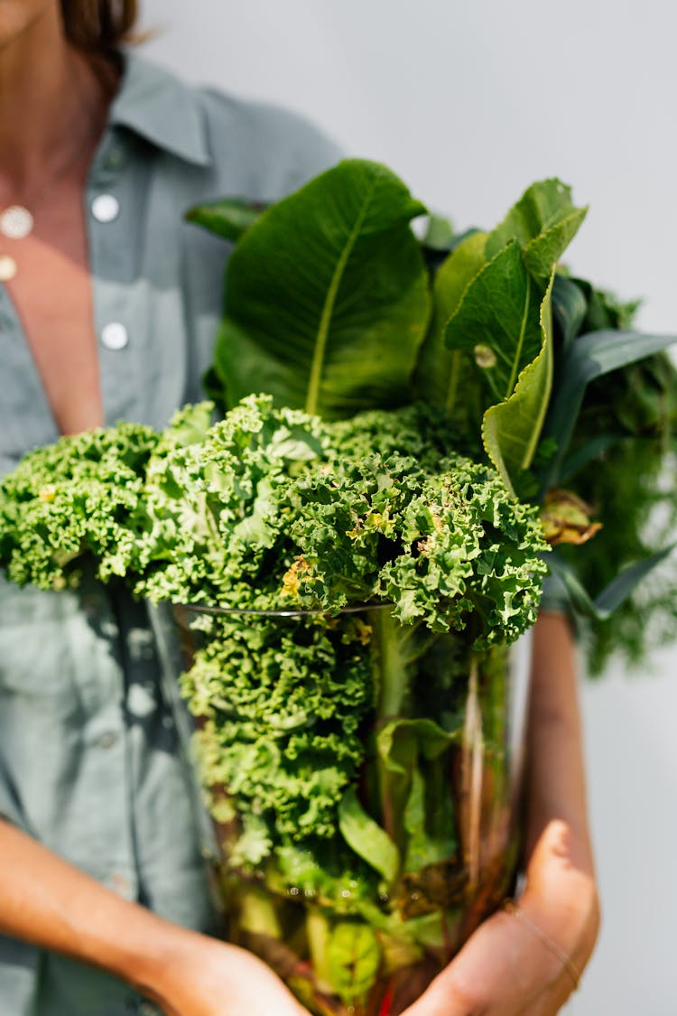 Unrecognizable Woman Holding Glass Vase With Green Vegetables