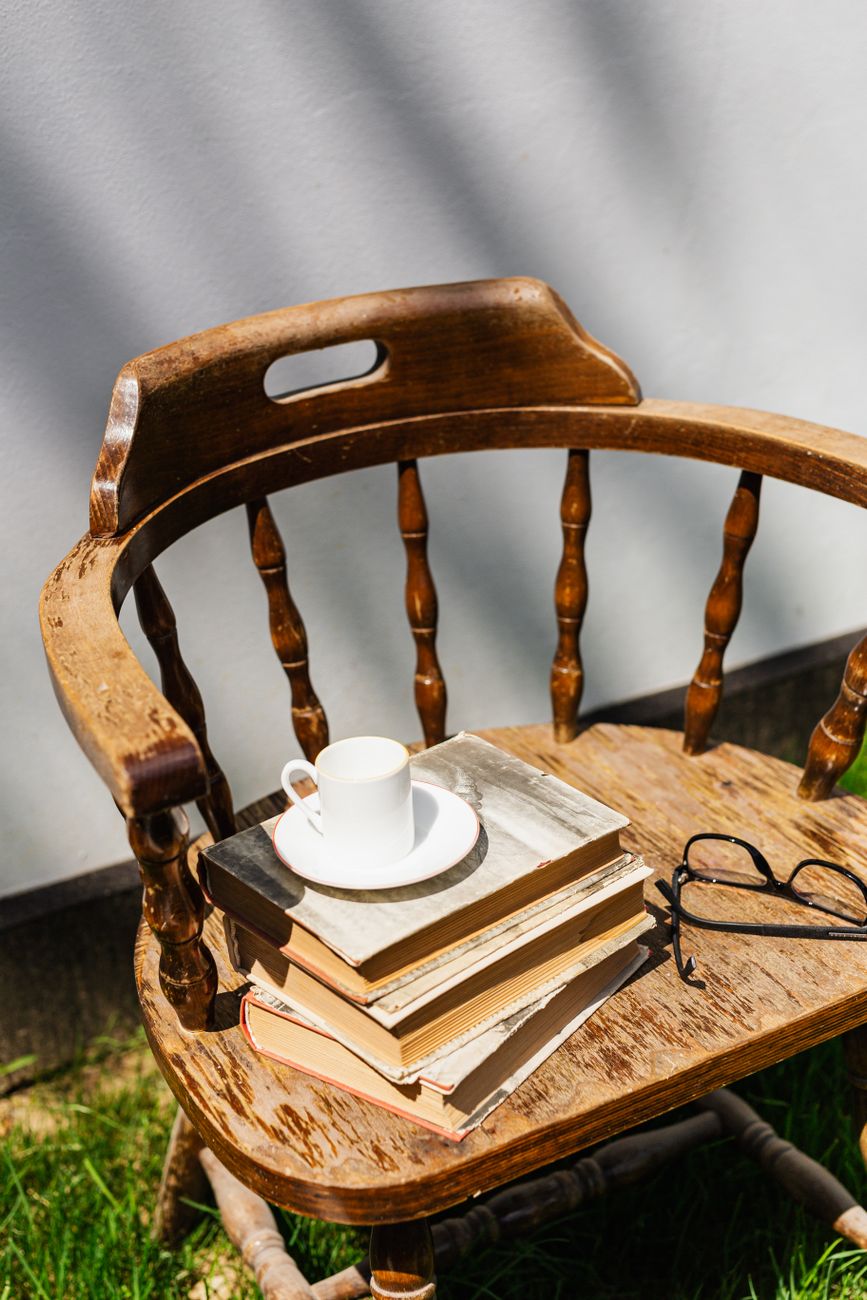 Rustic wooden chair with books, eyeglasses, and coffee cup in outdoor setting.