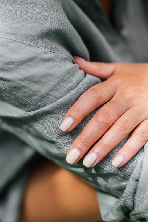 Free Close-up of a woman's hand with manicured nails gently resting on a linen sleeve. Stock Photo
