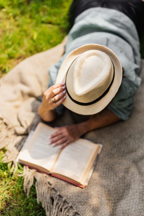 Free Woman lying on blanket outdoors reading a book, enjoying summer leisure time. Stock Photo