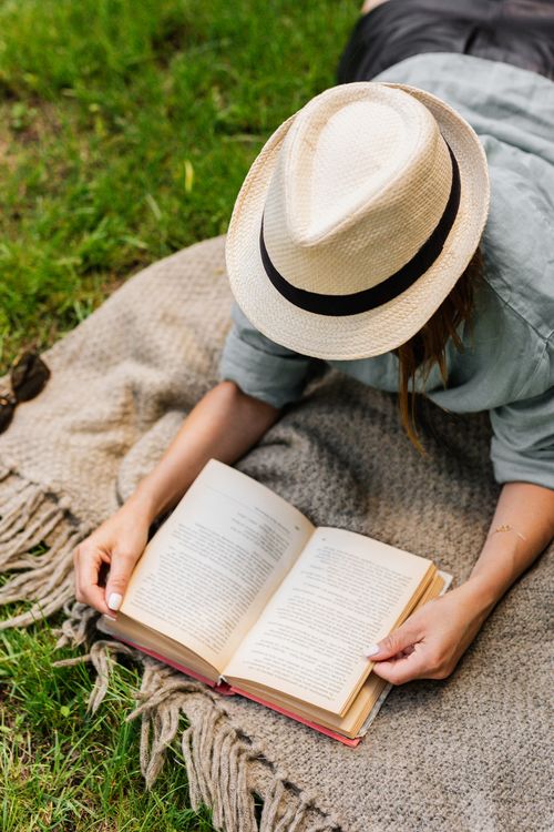 Free A woman enjoying reading on a blanket outdoors during summer, capturing relaxation and leisure. Stock Photo